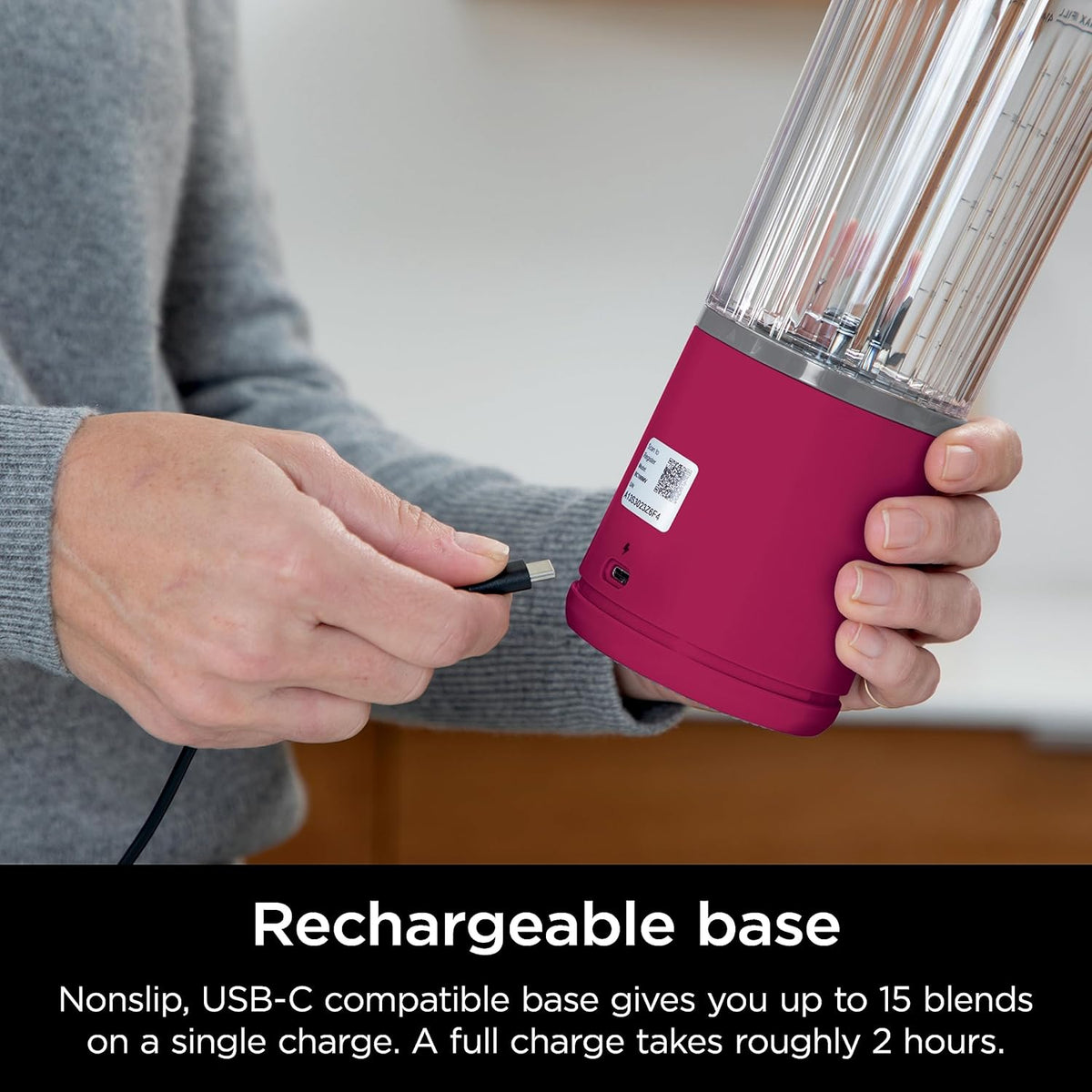 Magenta portable smoothie blender in hand with clear blending jar