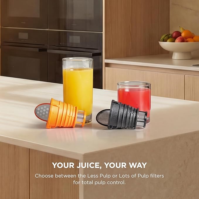 Cold press juicer with orange and black juice containers and filter parts on a counter