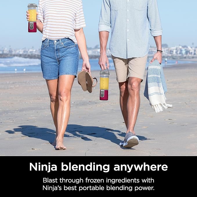 Portable smoothie blender held in hand with magenta body and clear jar
