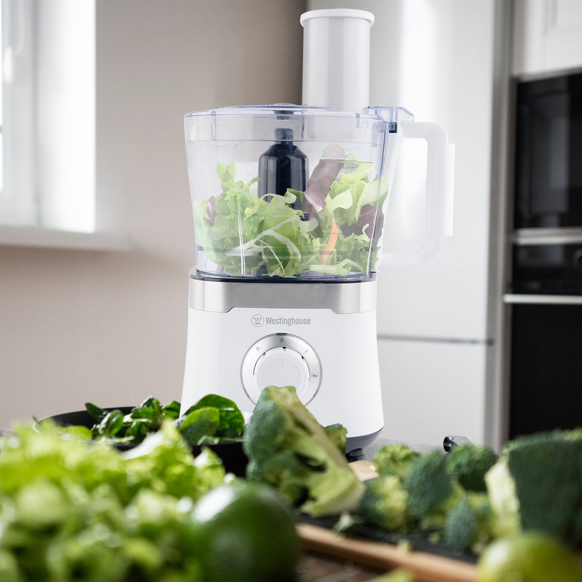 White Westinghouse food processor with clear bowl processing leafy greens