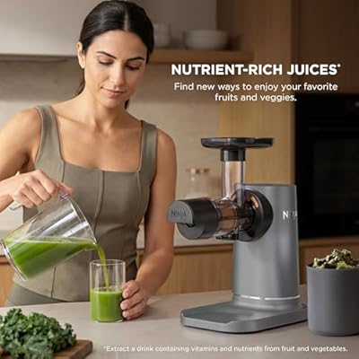 Cold press juicer with large feed chute and pulp cup base, shown dispensing green juice