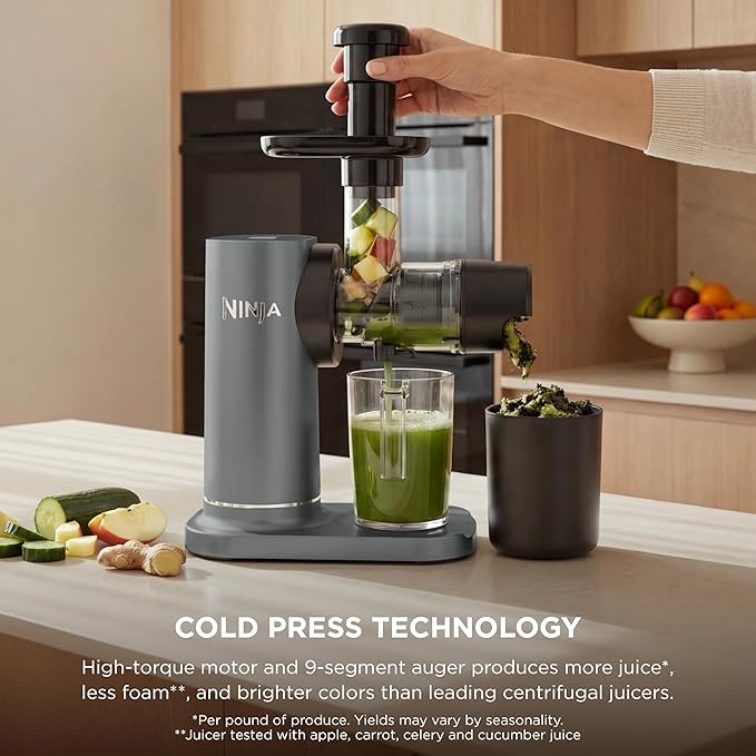Cold press juicer with hand placed on the hopper and clear container holding green juice