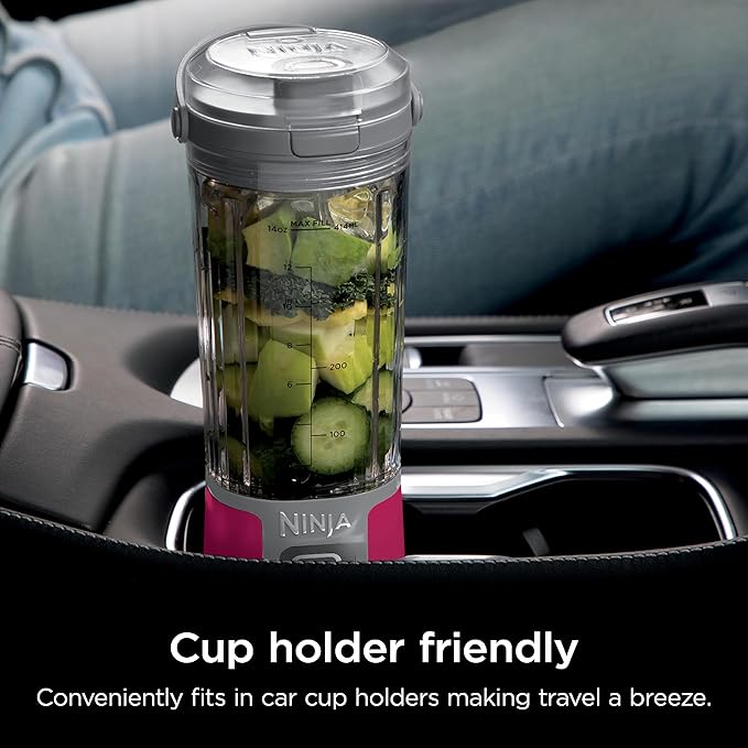 Portable smoothie blender with clear jar and magenta base in a vehicle cup holder