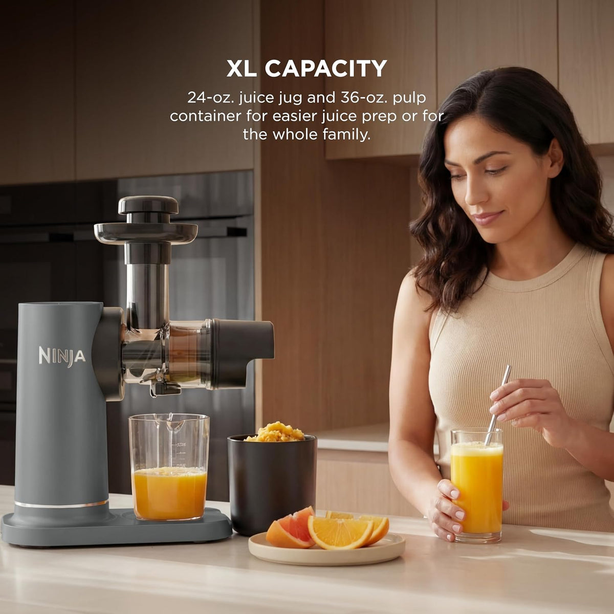 Cold press juicer with stainless body and juice container, next to a glass of orange juice