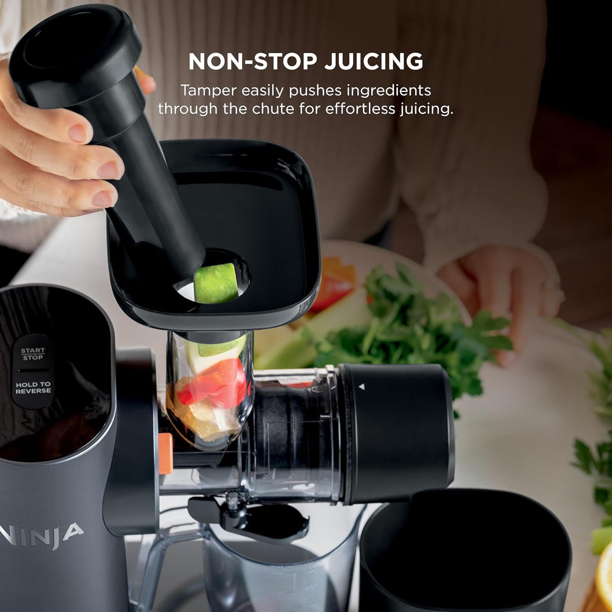 Cold press juicer with clear feed chamber and black pusher inserting produce into the chute