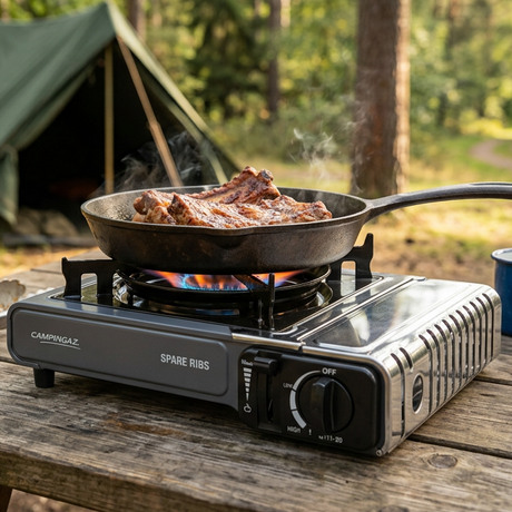 Portable camping stove with burner and control knobs, featuring a frying pan on top
